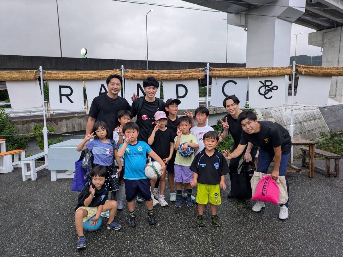 ロボス箕面の集合写真。RANDCの看板前で子どもたちとコーチが並んでいる